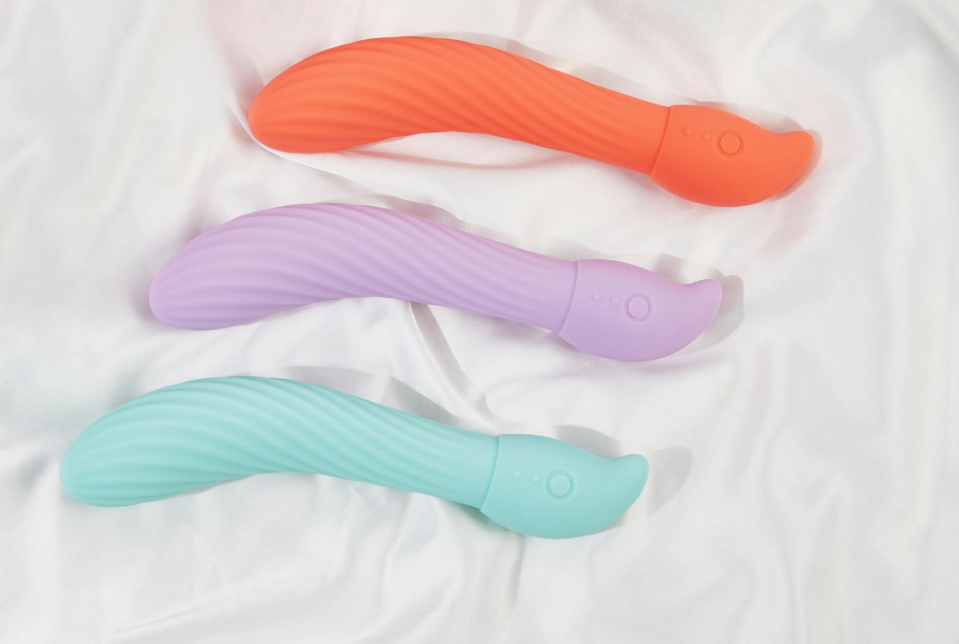 Three colorful clitoral vibrators arranged on white fabric, representing sensory pleasure and nervous system regulation.