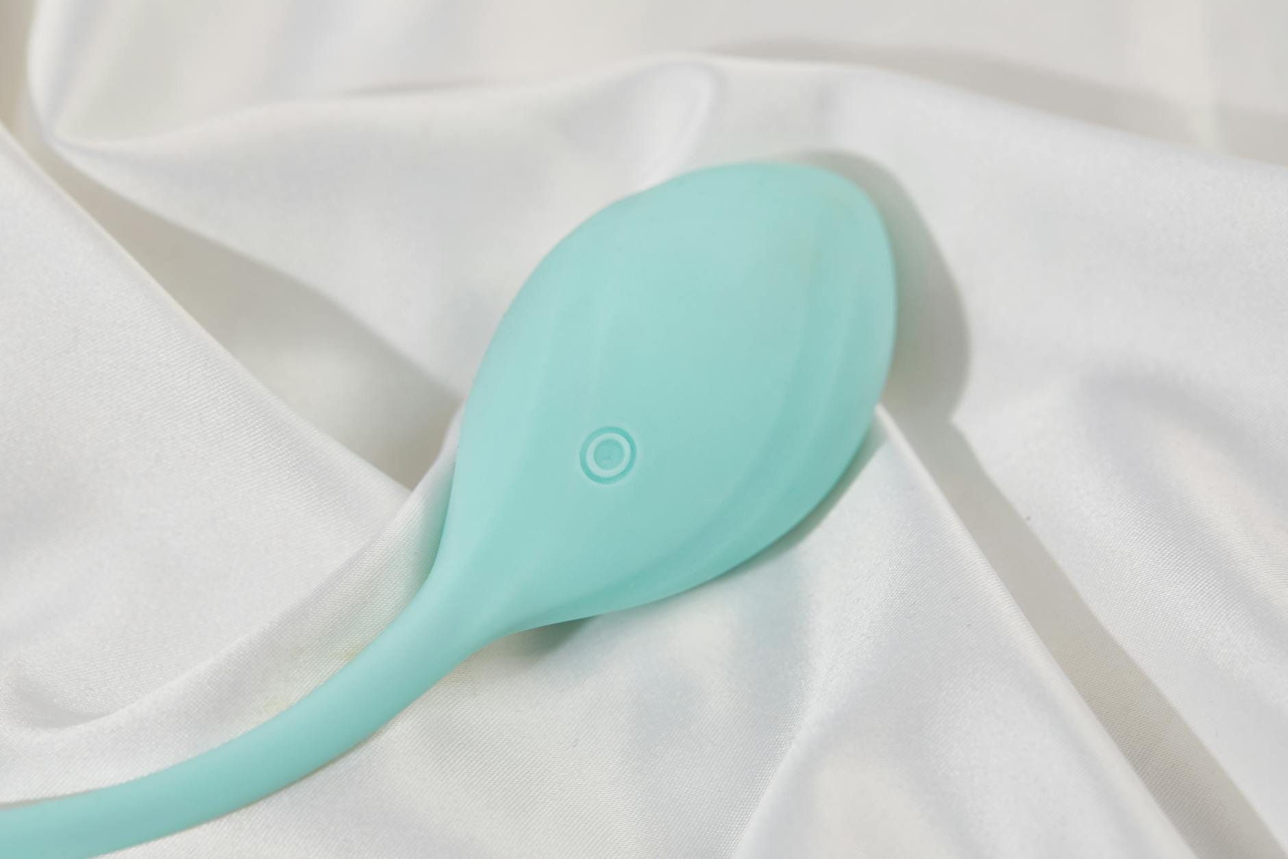 A sleek teal vibrator on soft white fabric, symbolizing gentle pleasure during recovery