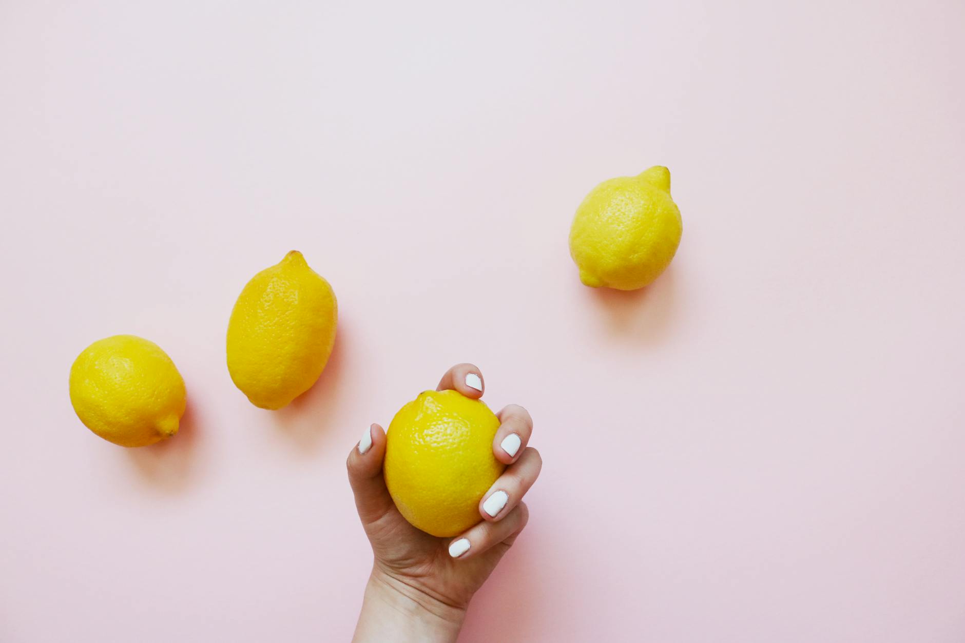 A hand holding a fresh lemon on a soft pink background, representing the bright, uncomplicated approach to pleasure.