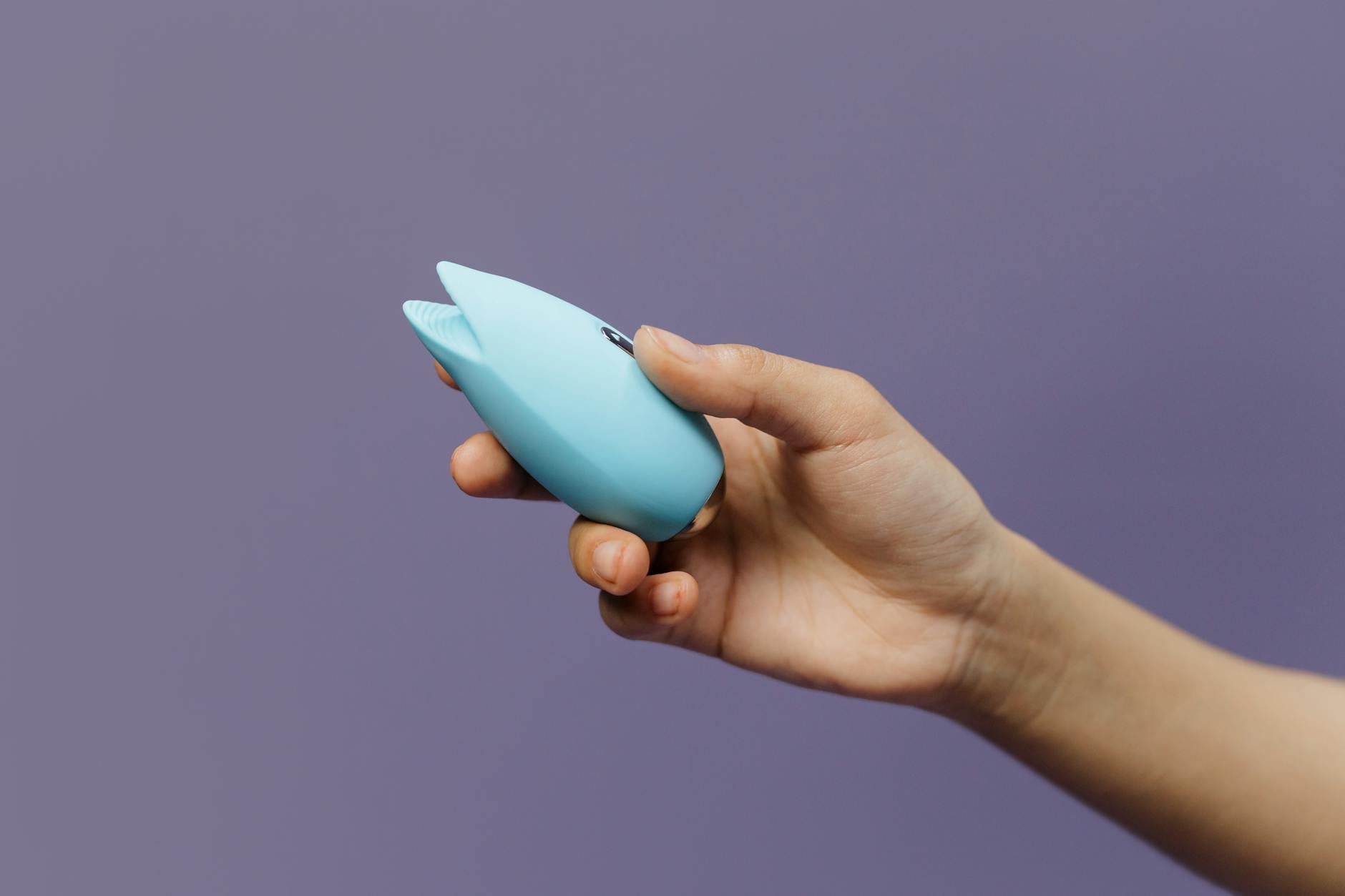 A hand holding a blue silicone vibrator against a purple background, representing comfort and self-care in intimate moments