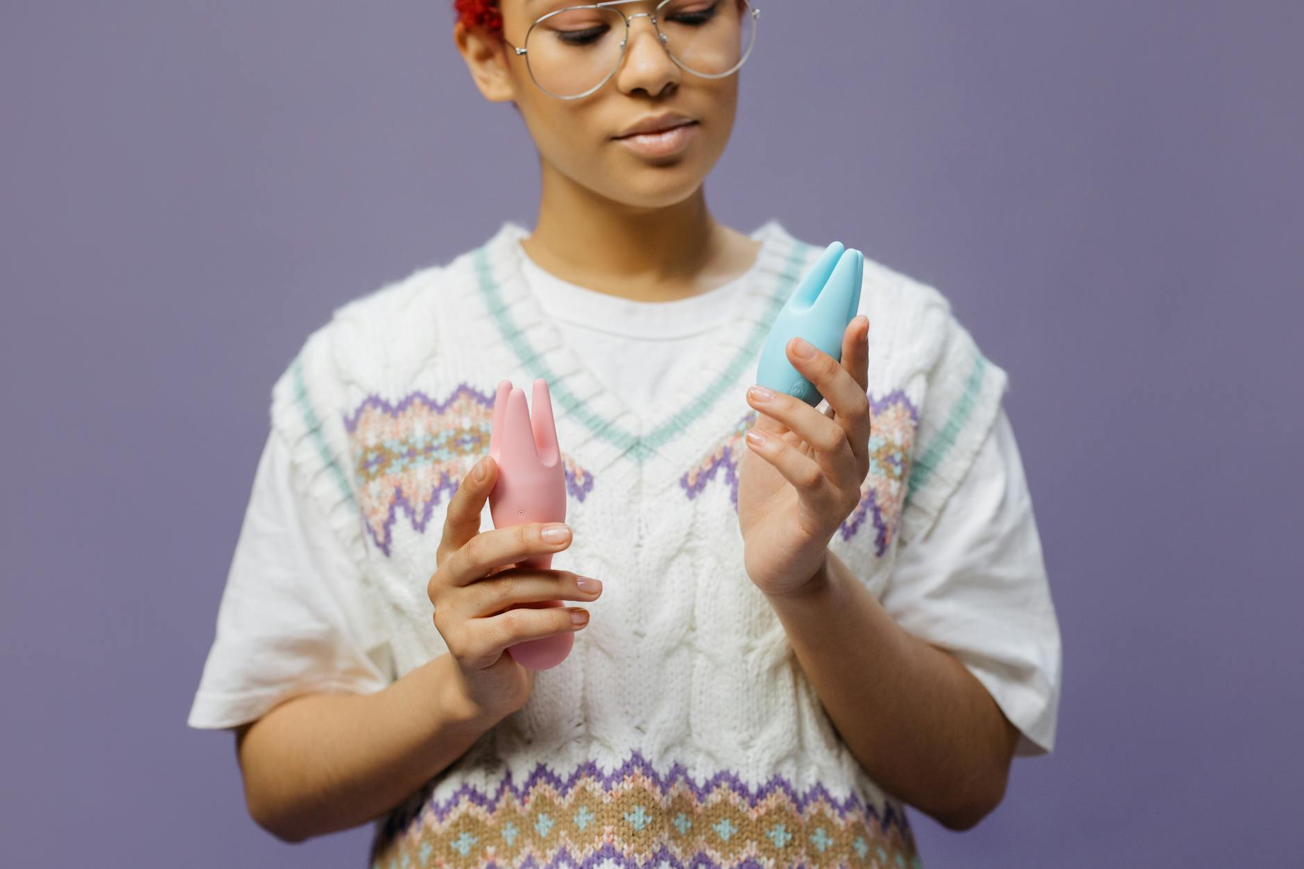 Person thoughtfully holding blue and pink vibrators, considering options for intimate wellness