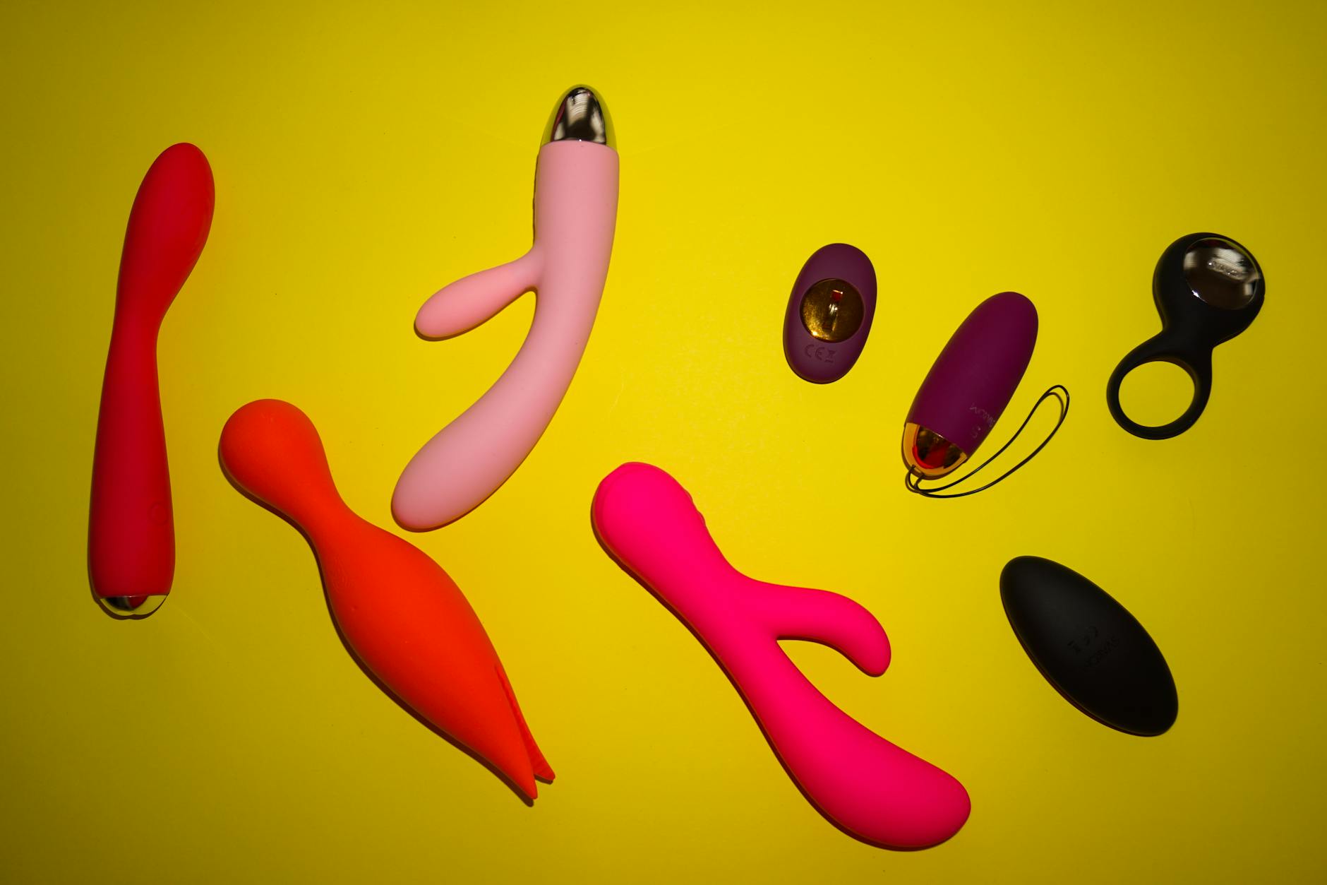 Colorful clitoral vibrators and adult toys arranged on a bright yellow surface