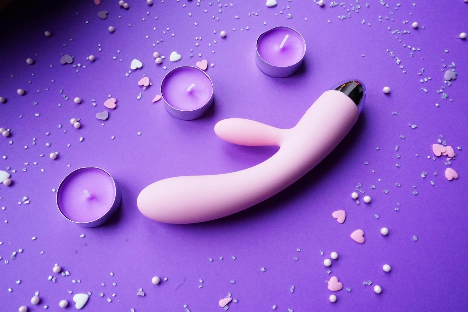 Pink lemon clitoral vibrator displayed on purple background with heart confetti and candles